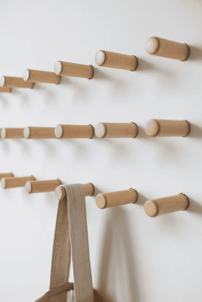 Simple cylindrical untreated maple dowel pegs mounted individually on a pure white wall in a loose grid pattern. The raw pale wood shows minimal grain. One lightweight linen bag hangs from a single peg. Extremely bright, airy Nordic light flooding the space. Maximum simplicity, serene and spacious composition.