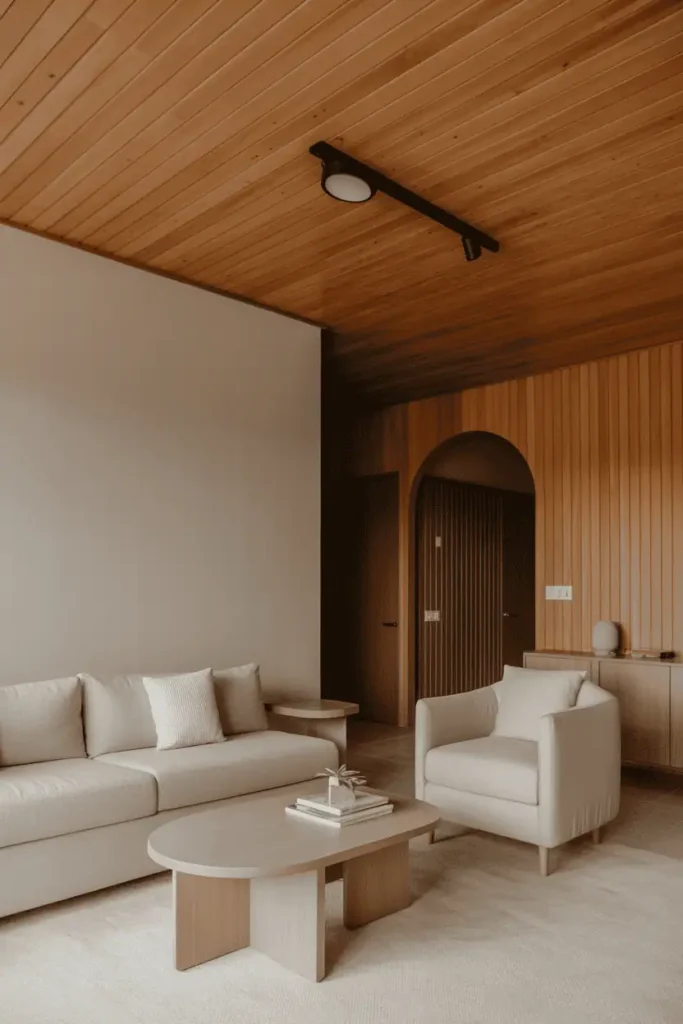 Living room featuring wood-paneled ceiling, light wood tones, neutral walls, minimal furniture, soft overhead lighting, cozy architectural atmosphere, Scandinavian–modern wood aesthetic, realistic interior photography, high resolution, no people, no text, no watermark
